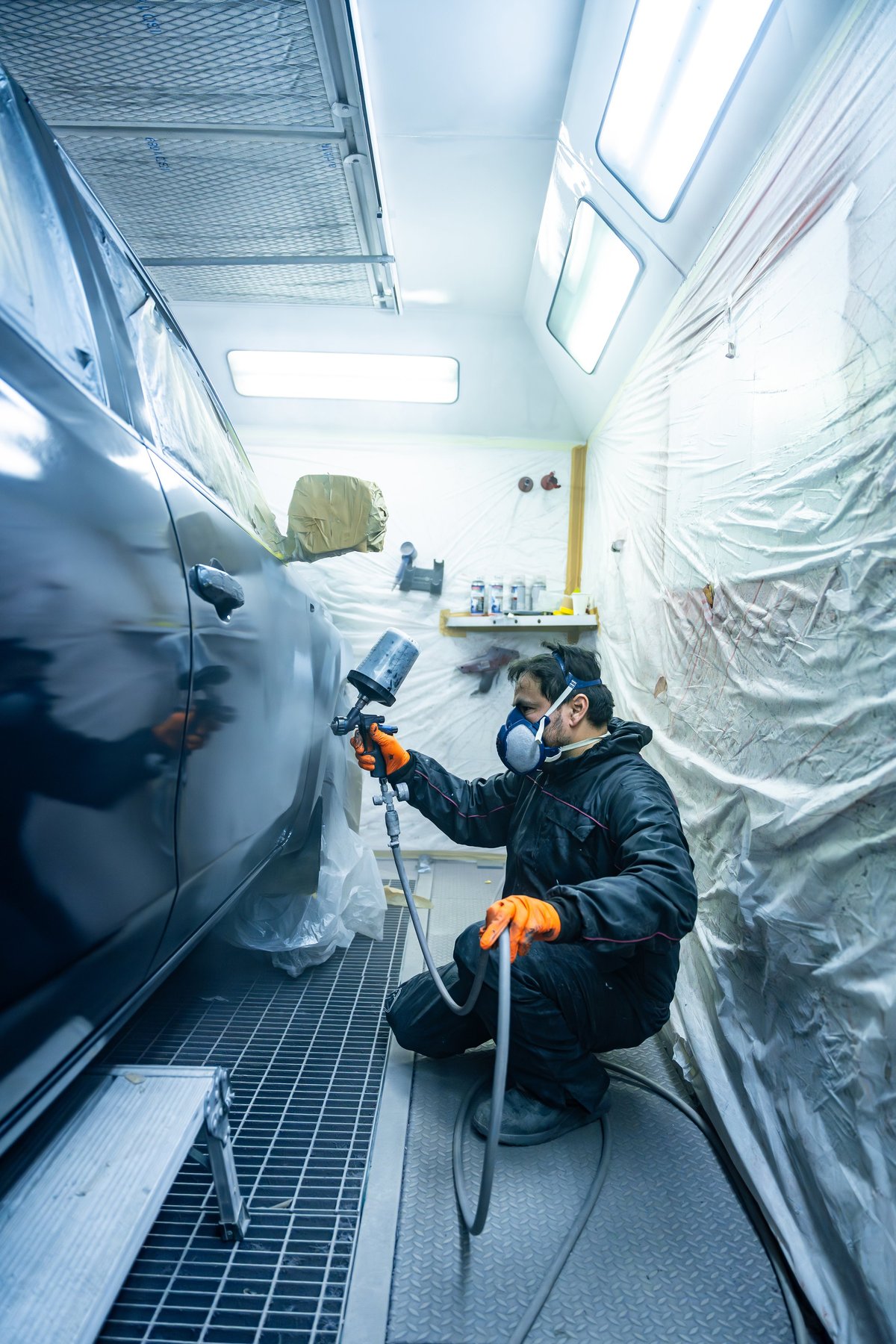 Technician applying fresh paint to a vehicle in a professional spray booth